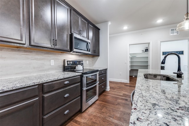 kitchen featuring decorative backsplash, crown molding, appliances with stainless steel finishes, a sink, and baseboards