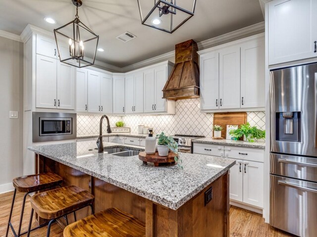 kitchen with ornamental molding, a chandelier, custom range hood, light wood-style flooring, and appliances with stainless steel finishes