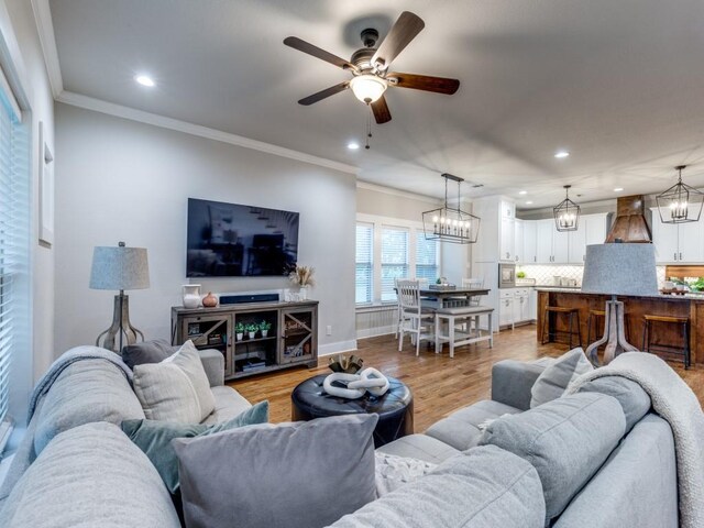 living room featuring recessed lighting, crown molding, ceiling fan with notable chandelier, and light wood-type flooring