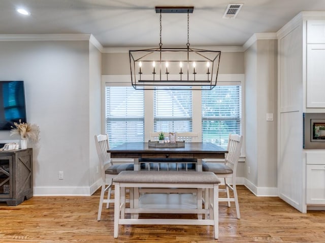 dining area with light wood-style floors, baseboards, crown molding, and visible vents