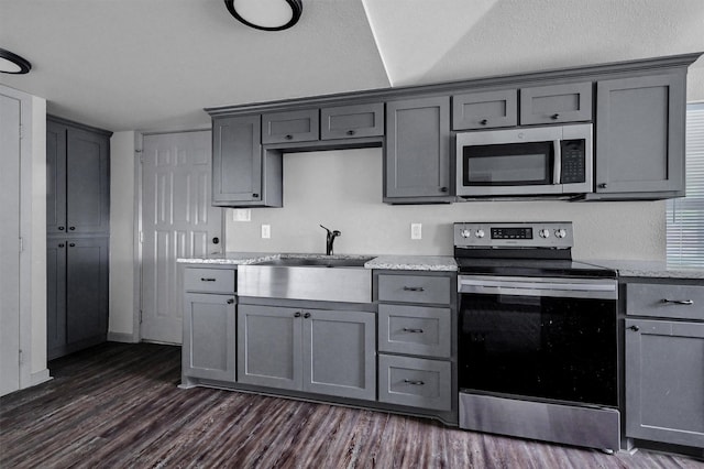 kitchen featuring light stone countertops, dark wood-type flooring, a sink, appliances with stainless steel finishes, and gray cabinetry
