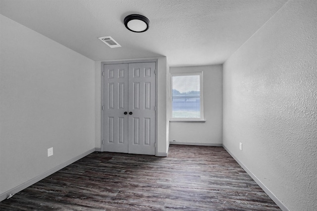 unfurnished bedroom with visible vents, a closet, dark wood-style flooring, a textured wall, and baseboards