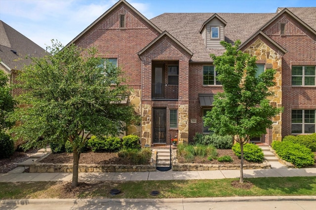 townhome / multi-family property featuring brick siding, stone siding, and roof with shingles