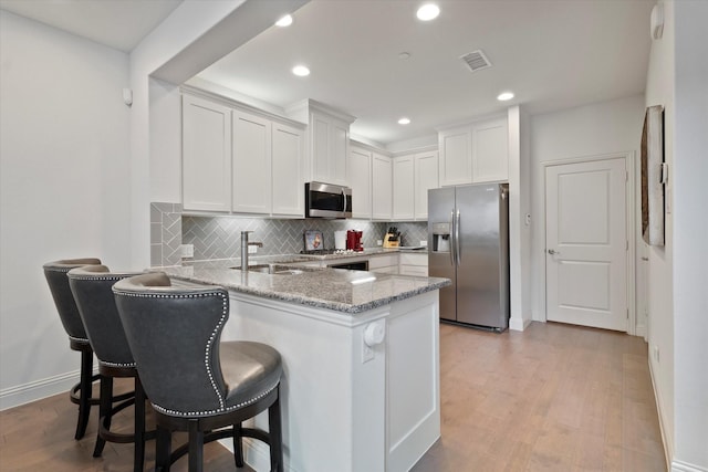 kitchen featuring visible vents, a peninsula, light stone counters, a sink, and appliances with stainless steel finishes