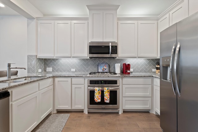 kitchen with light wood-type flooring, white cabinets, tasteful backsplash, a sink, and stainless steel appliances