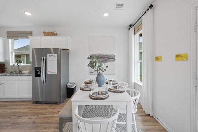 kitchen with stainless steel refrigerator with ice dispenser, white cabinetry, a sink, and light wood finished floors
