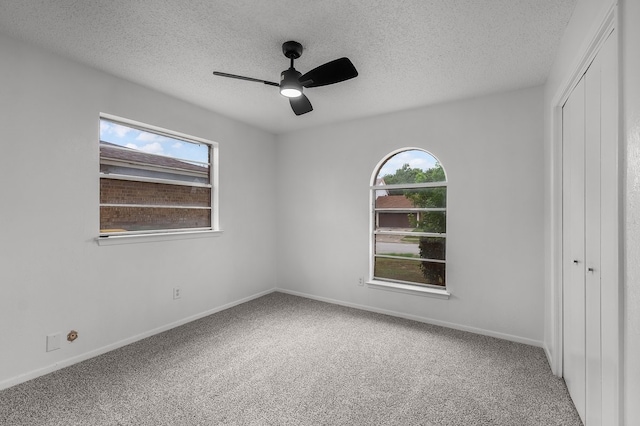 interior space with carpet flooring, a ceiling fan, a textured ceiling, and baseboards