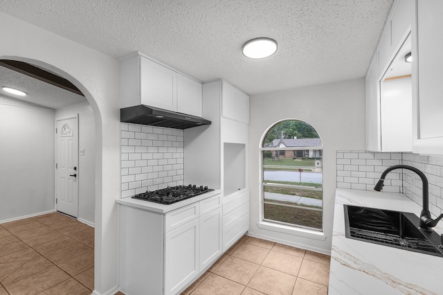 kitchen featuring a textured ceiling, white cabinetry, a sink, light tile patterned floors, and black gas cooktop