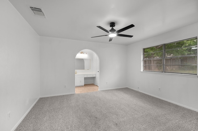 spare room featuring ceiling fan, light colored carpet, arched walkways, baseboards, and visible vents