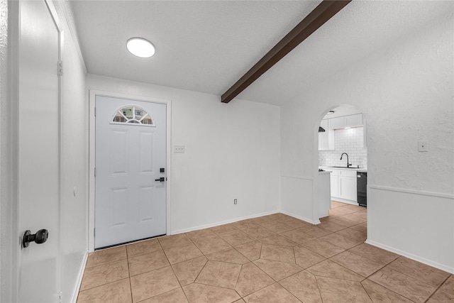 entrance foyer with arched walkways, light tile patterned floors, and beam ceiling