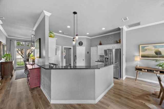 kitchen featuring white cabinets, crown molding, stainless steel fridge, dark stone countertops, and visible vents