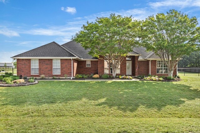view of front of property with brick siding, fence, a front yard, and roof with shingles