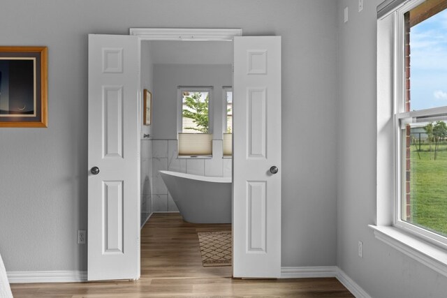 bathroom featuring a freestanding bath, baseboards, and wood finished floors