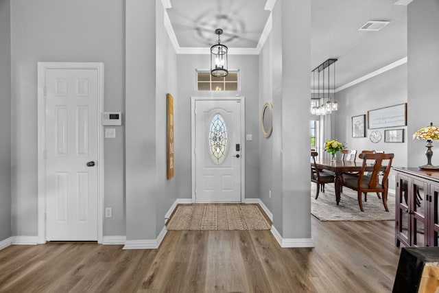 foyer featuring baseboards, ornamental molding, wood finished floors, and visible vents