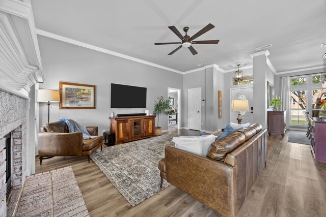 living area with crown molding, ceiling fan, a fireplace, wood finished floors, and visible vents