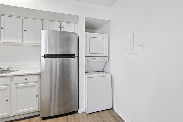 interior space with laundry area, electric panel, a textured ceiling, stacked washer / dryer, and light wood finished floors