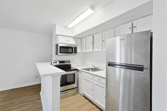 kitchen featuring a textured ceiling, light wood-type flooring, a sink, stainless steel appliances, and white cabinetry