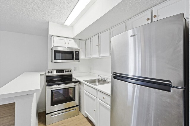 kitchen with white cabinets, appliances with stainless steel finishes, a sink, light countertops, and a peninsula