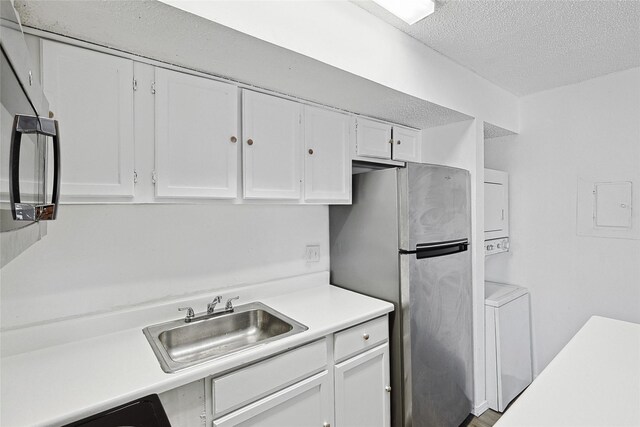 kitchen featuring white cabinets, stacked washer and dryer, a sink, light countertops, and a textured ceiling