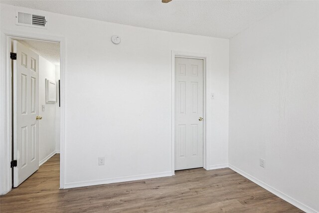 empty room featuring baseboards, a textured ceiling, visible vents, and wood finished floors