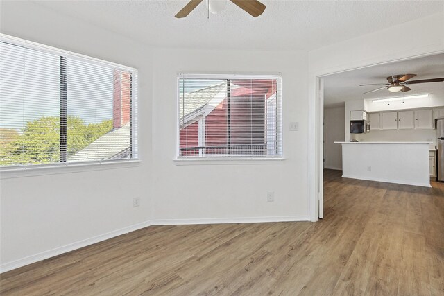 interior space featuring baseboards, a ceiling fan, wood finished floors, and a wealth of natural light