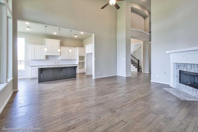 unfurnished living room featuring a ceiling fan, a high ceiling, dark wood finished floors, and a fireplace
