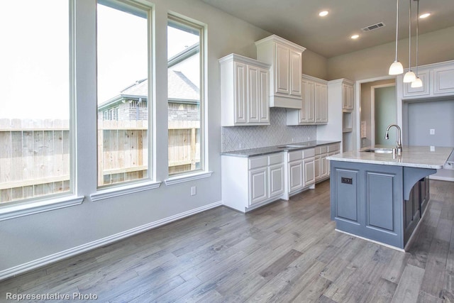 kitchen with white cabinets, a sink, light wood-style flooring, backsplash, and visible vents