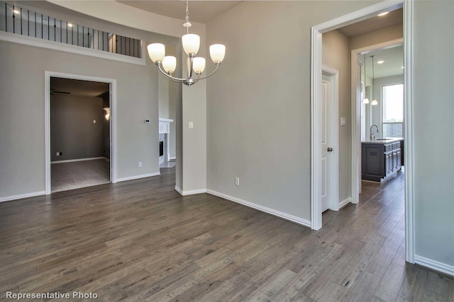 unfurnished dining area featuring an inviting chandelier, a sink, dark wood finished floors, and baseboards