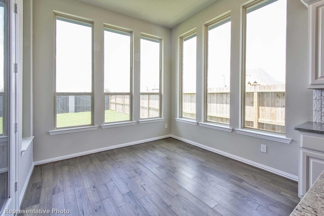 unfurnished sunroom featuring baseboards and wood finished floors