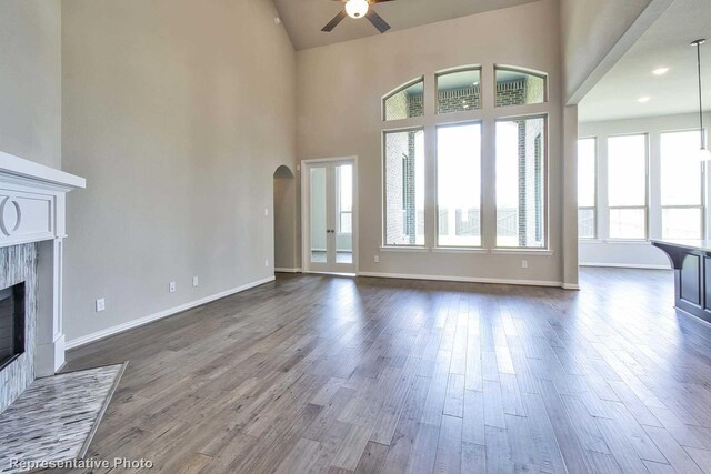 unfurnished living room with a premium fireplace, ceiling fan, arched walkways, and dark wood-type flooring