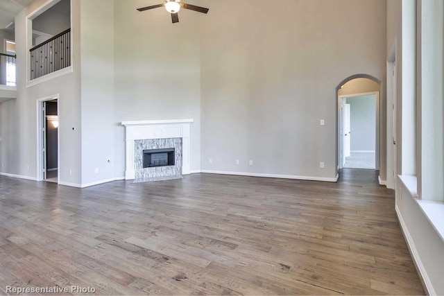 unfurnished living room with a high end fireplace, arched walkways, a high ceiling, and a ceiling fan