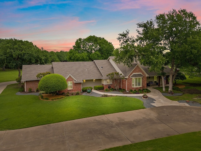 view of front of property featuring roof with shingles, a front lawn, and brick siding