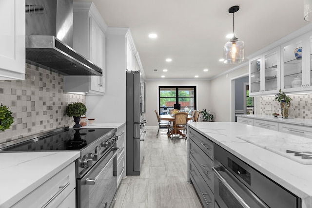 kitchen featuring wall chimney range hood, crown molding, tasteful backsplash, stainless steel appliances, and white cabinetry