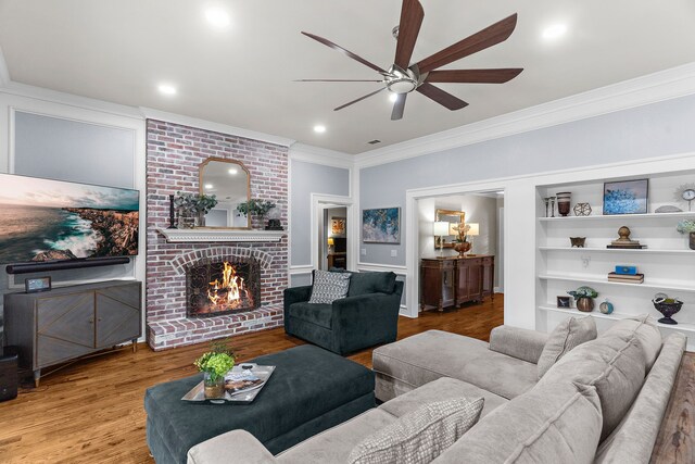 living room with ornamental molding, wood finished floors, a fireplace, ceiling fan, and built in shelves