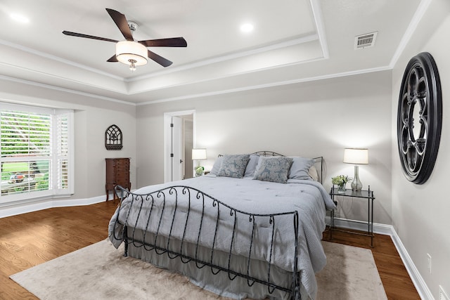 bedroom with visible vents, wood finished floors, baseboards, ornamental molding, and a tray ceiling