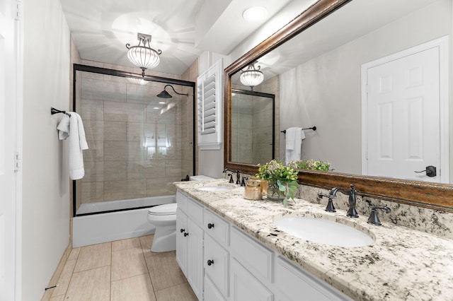bathroom with double vanity, a sink, combined bath / shower with glass door, and toilet