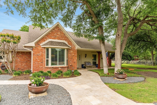view of front facade featuring brick siding, fence, and a shingled roof