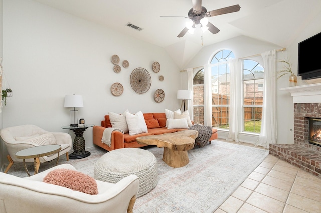 living room featuring ceiling fan, a brick fireplace, light tile patterned floors, vaulted ceiling, and visible vents