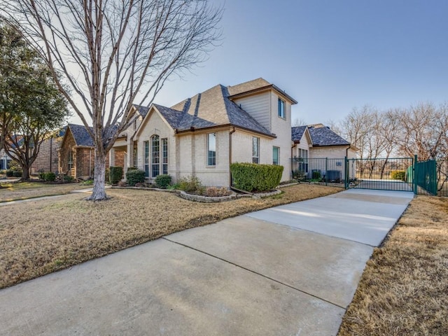 view of side of home featuring fence, a shingled roof, brick siding, a gate, and driveway