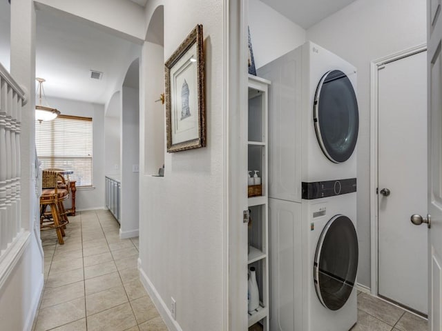laundry room with laundry area, visible vents, arched walkways, stacked washing maching and dryer, and light tile patterned flooring