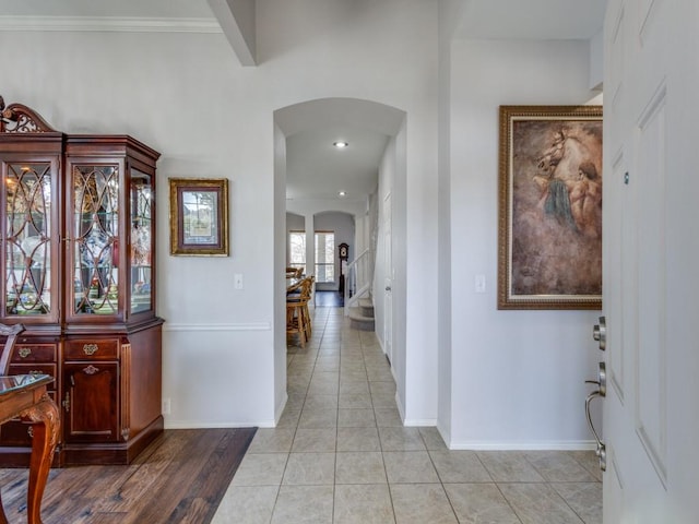 hallway with stairway, arched walkways, baseboards, and light tile patterned flooring