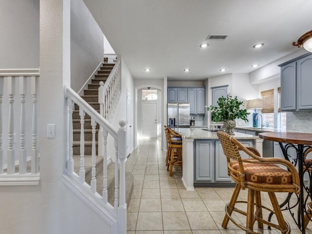 kitchen featuring light tile patterned flooring, decorative backsplash, a healthy amount of sunlight, stainless steel refrigerator with ice dispenser, and gray cabinetry