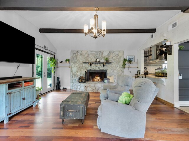 living room with a notable chandelier, lofted ceiling with beams, a stone fireplace, wood finished floors, and visible vents