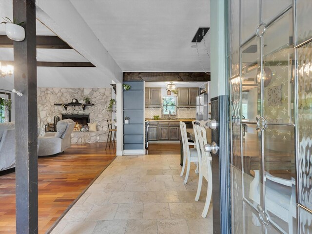 interior space featuring a stone fireplace, beam ceiling, a healthy amount of sunlight, and stone tile flooring