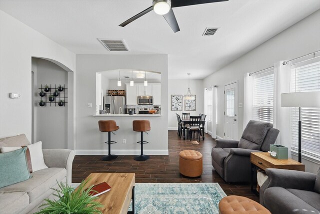 living room with arched walkways, ceiling fan, dark wood-style flooring, and visible vents