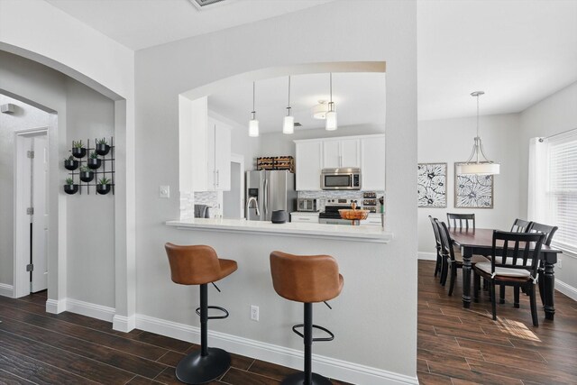 kitchen with baseboards, dark wood-style floors, tasteful backsplash, arched walkways, and appliances with stainless steel finishes
