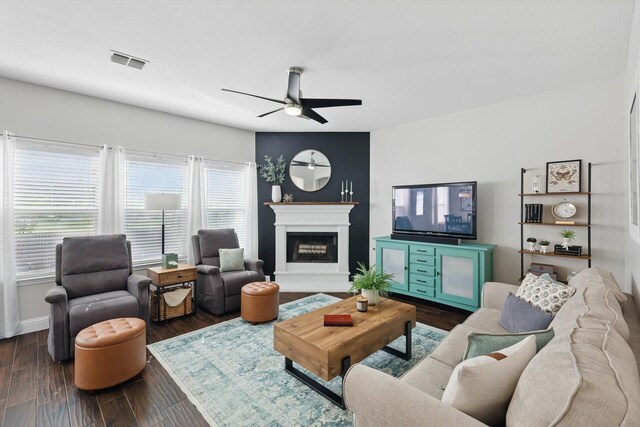 living area featuring ceiling fan, a fireplace with raised hearth, dark wood finished floors, baseboards, and visible vents