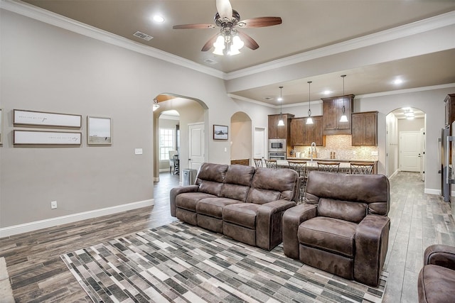 living room with visible vents, a ceiling fan, wood finished floors, baseboards, and arched walkways