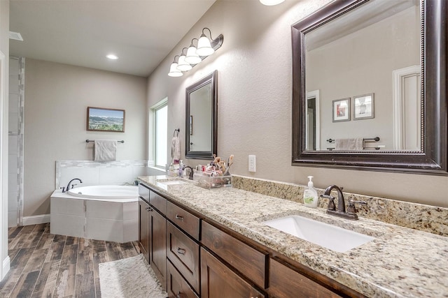 bathroom with double vanity, a sink, a bath, and wood finished floors