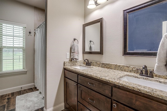 full bath with double vanity, a sink, baseboards, and wood finished floors